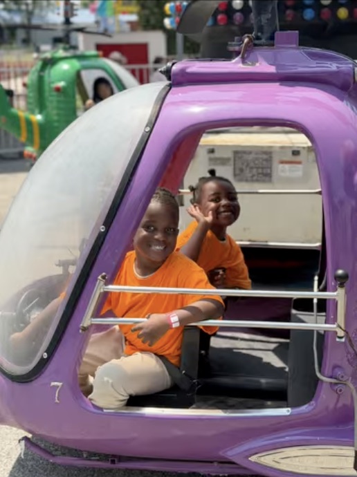 Two smiling children enjoying a purple amusement ride